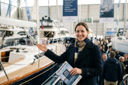 Femme souriante en manteau navy et foulard lors d'une exposition de yachts
